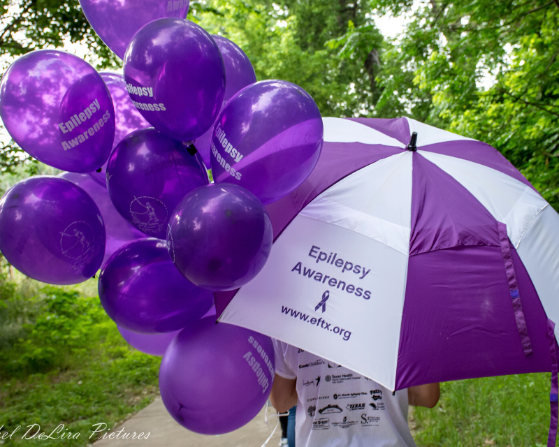 Purple and white umbrella and purple balloons that both say "Epilepsy Awareness"